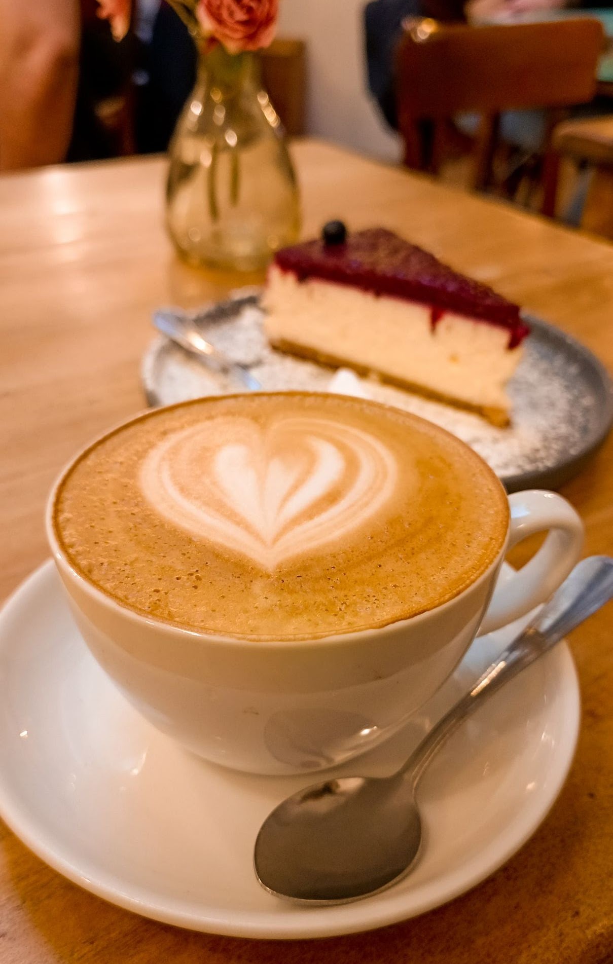 A cup of coffee with latte art and a slice of cheesecake on a table.